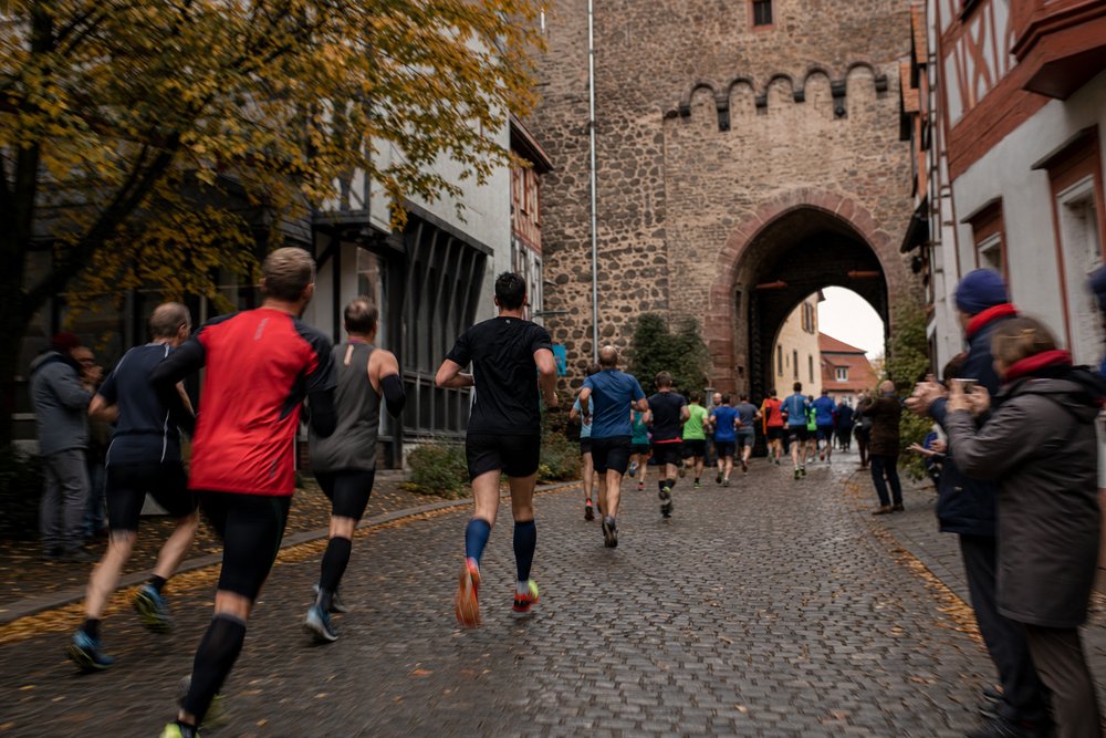 Läuferfeld auf Kopfsteinpflaster vor dem historischen Burgtor in der Friedberger Altstadt während eines Stadtlaufs