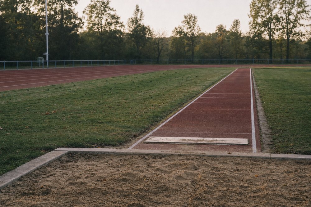 Weitsprunggrube mit Absprungbalken und rotbrauner Tartan-Anlaufbahn auf einer kommunalen Leichtathletik-Sportanlage im Grünen